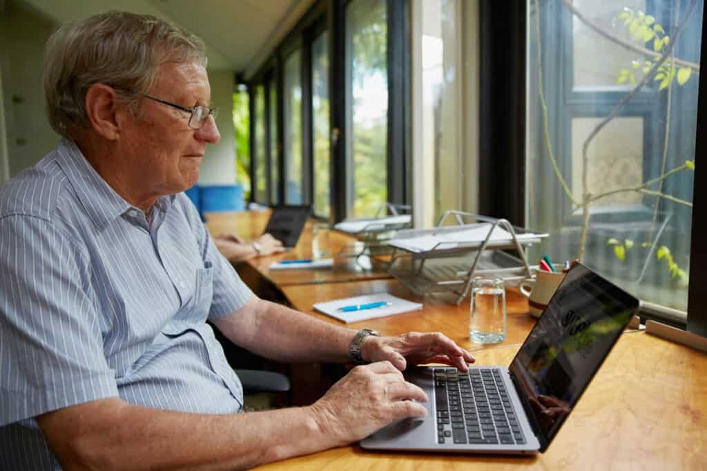 a man sitting at a table using a laptop computer to search for and apply to Canadian government grants